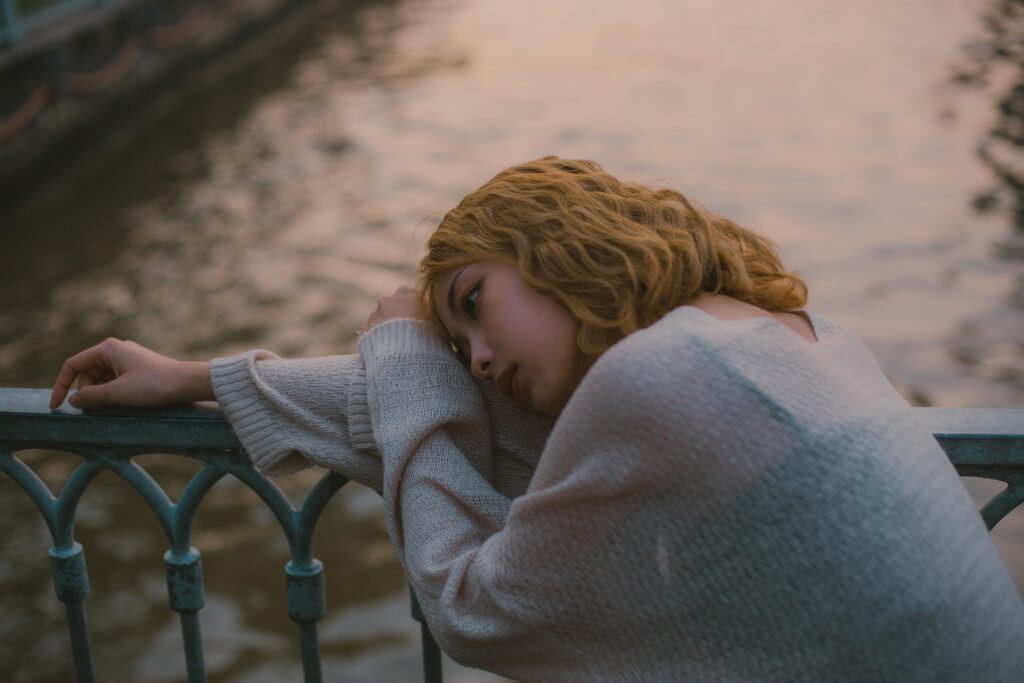 Woman sitting alone by the riverside, appearing lost in deep thoughts and stress